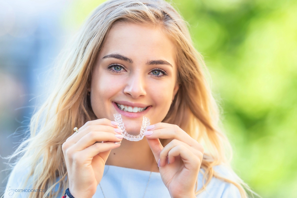 a woman smiling and holding invisalign clear aligners, one of the alternatives to braces in little falls, NJ