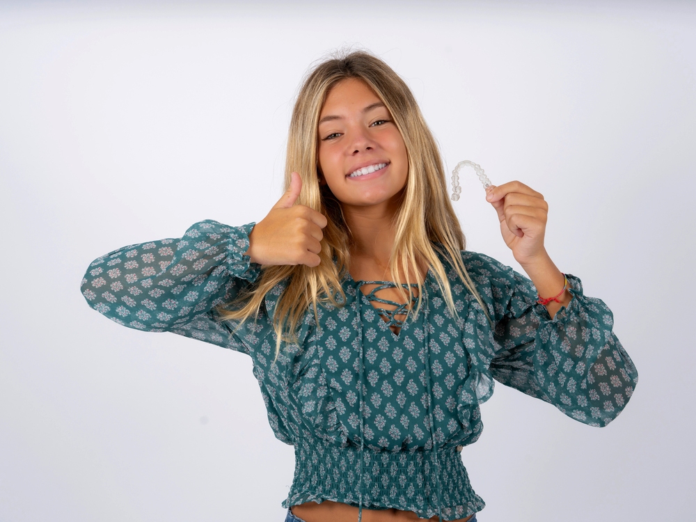 a woman smiling while holding invisalign after understanding Does Insurance Cover Invisalign in Little Falls and Metuchen, NJ?